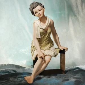 Statua in porcellana di donna in abito verde oliva con pizzo e scialle in tulle, seduta su panca scura.