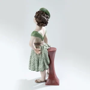 Statua in porcellana Maggie con gonna verde e bianca, cappello fascinator e tavolino bordeaux.