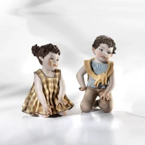 Statue in porcellana di bimba con abito a quadri gialli e bimbo con t-shirt azzurra e maglioncino giallo in ginocchio.