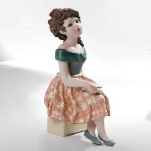 Statua in porcellana Manuela di Sibania, seduta con gonna rosa, bustino blu di prussia e pochette in grembo.
