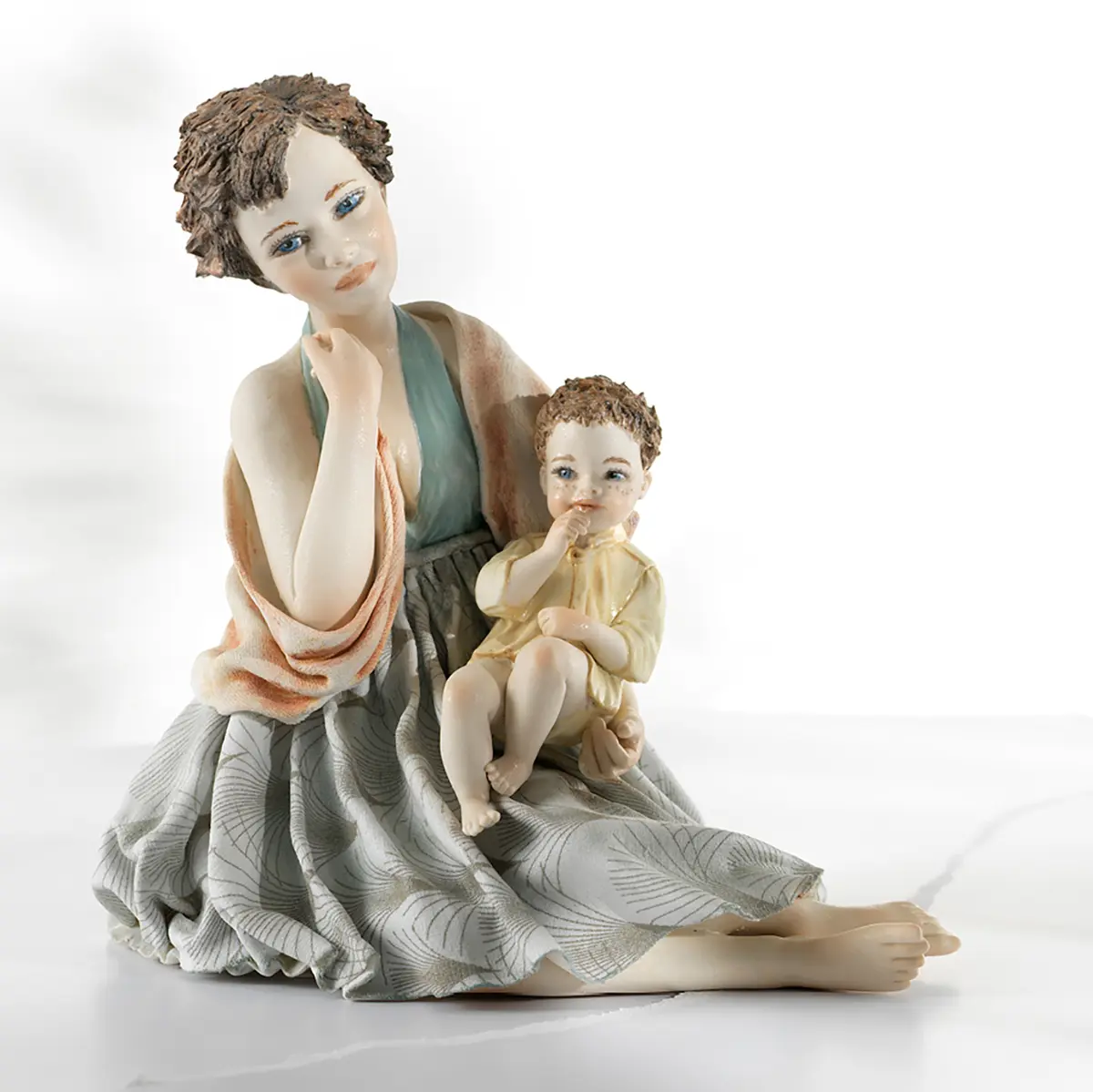 Statua in porcellana con mamma in abito azzurro e scialle salmone che tiene in braccio il suo bimbo in camiciola gialla.