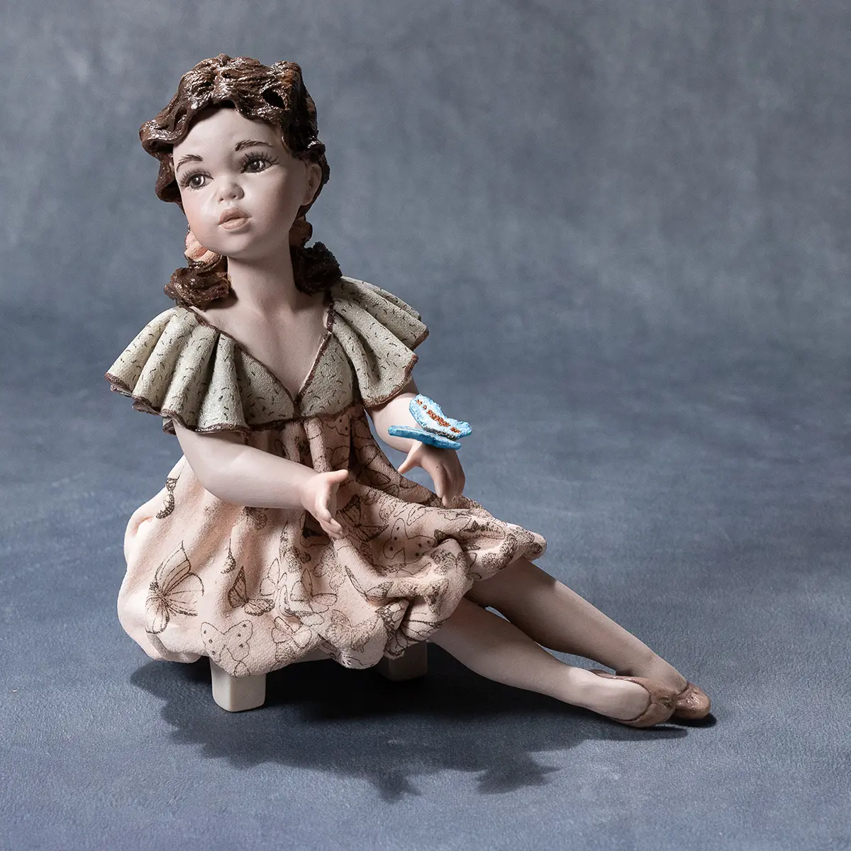 Statua in porcellana Michela in posa da ballerina con abito svolazzante e farfalla azzurra sulla mano.