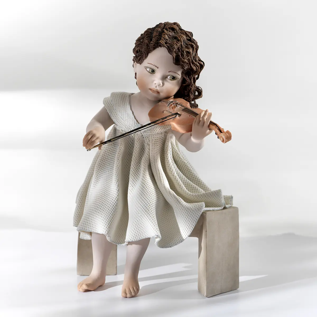 Statua in porcellana di ragazza in abito di tulle che suona il violino seduta su panca marmorizzata.
