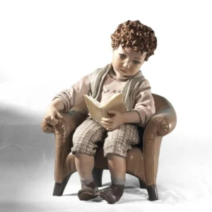 Statua in porcellana di Sibania con bimbo seduto su poltrona, maglioncino salmone a rombi e libro di poesie aperto sulle gambe.