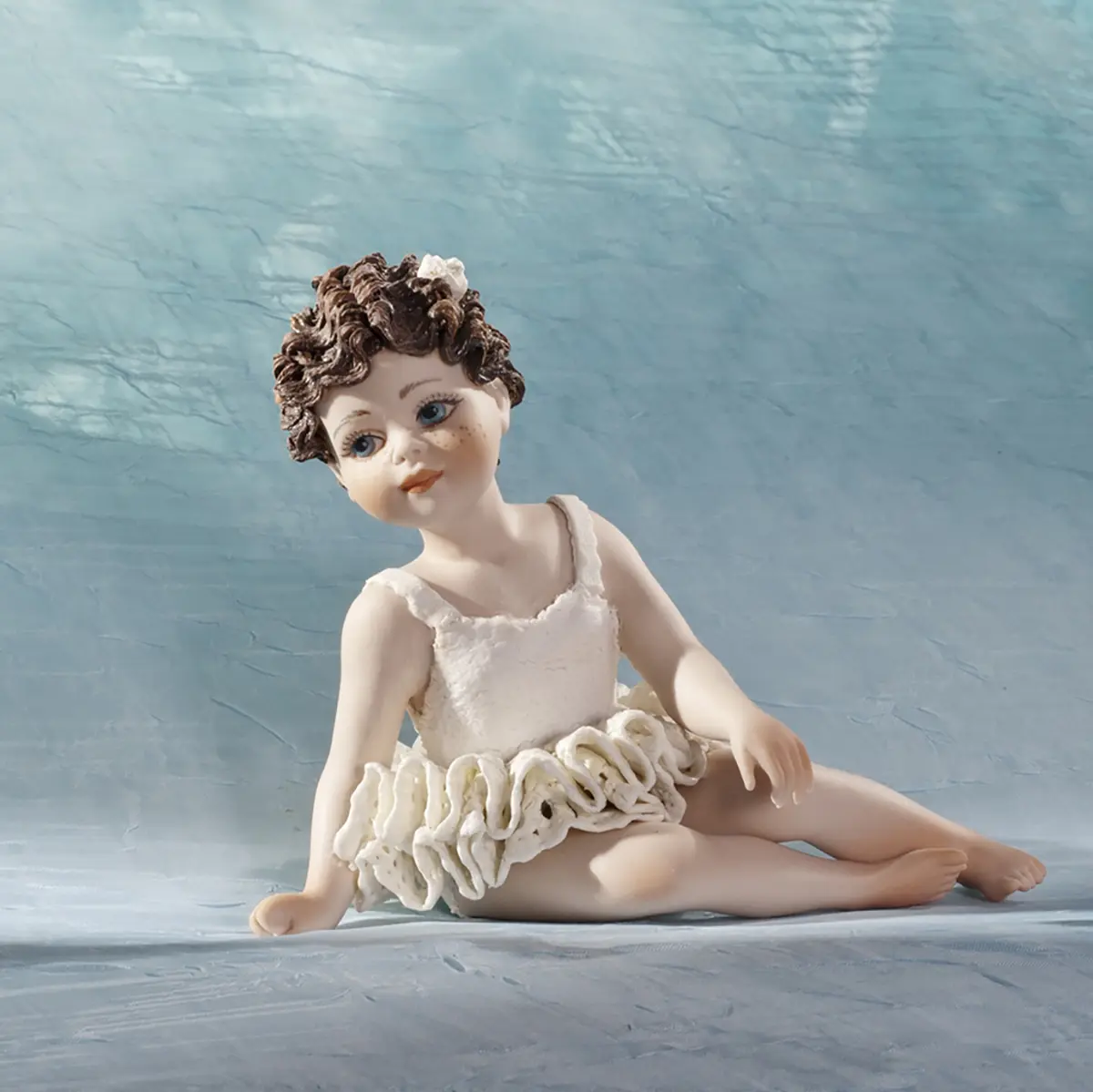 Statua in porcellana di bimba ballerina in tutù di pizzo, seduta a terra con fiocco bianco nei capelli.