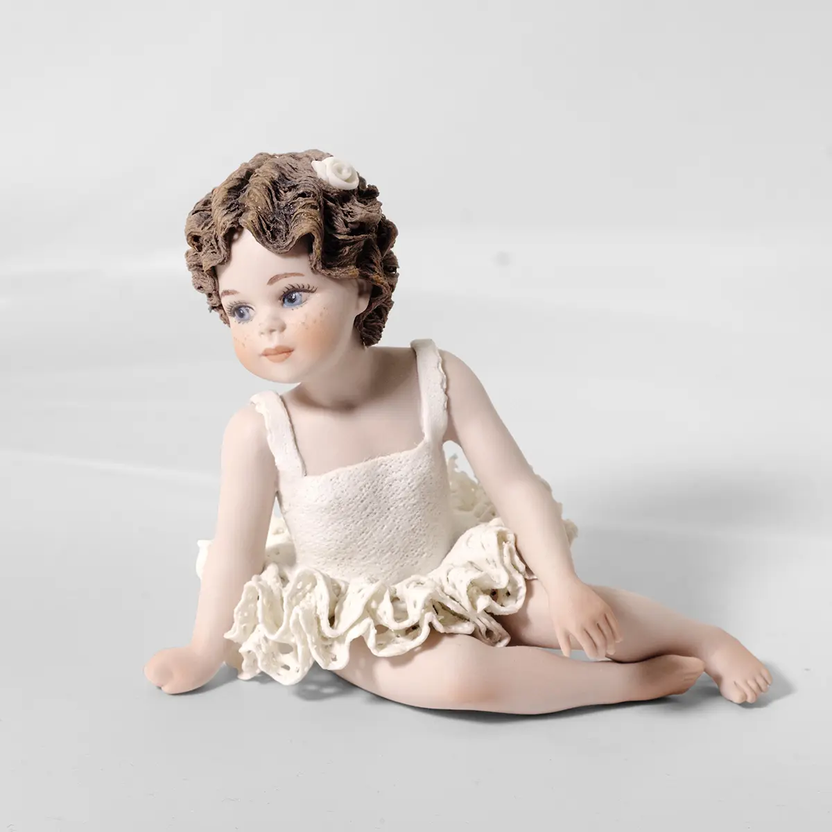 Statua in porcellana di bimba ballerina in tutù di pizzo, seduta a terra con fiocco bianco nei capelli.