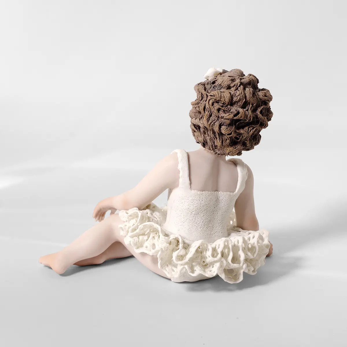 Statua in porcellana di bimba ballerina in tutù di pizzo, seduta a terra di lato con fiocco bianco tra i capelli.