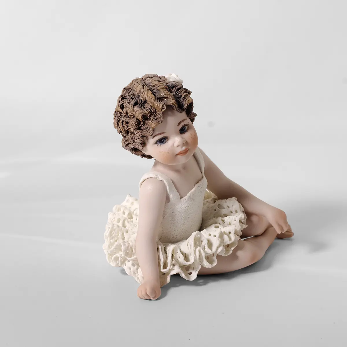 Statua in porcellana di bimba ballerina in tutù di pizzo, seduta a terra con le gambe di lato e fiocco bianco.