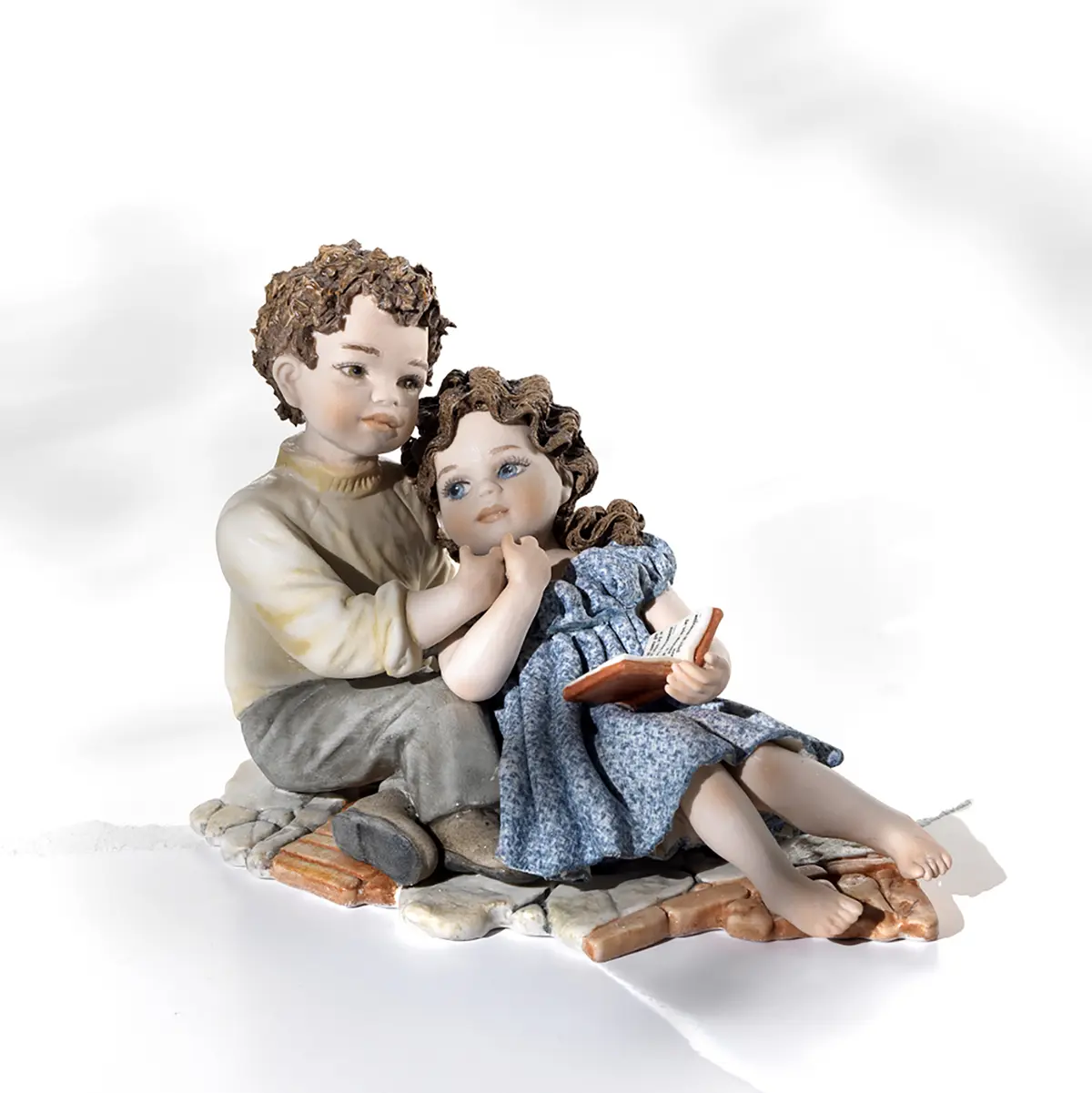 Statua in porcellana di fidanzatini stesi su un selciato abbracciati e per mano, lui in maglia beige e lei in abitino blu.