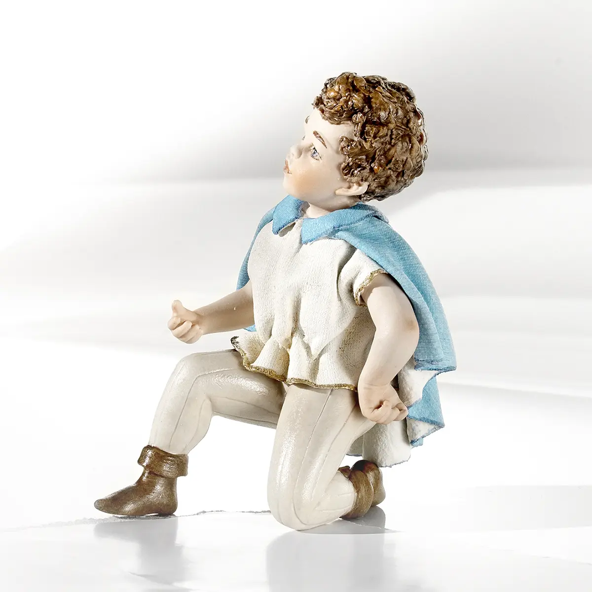Statua in porcellana del Principe Azzurro in ginocchio, con casacca bianca e mantello azzurro.