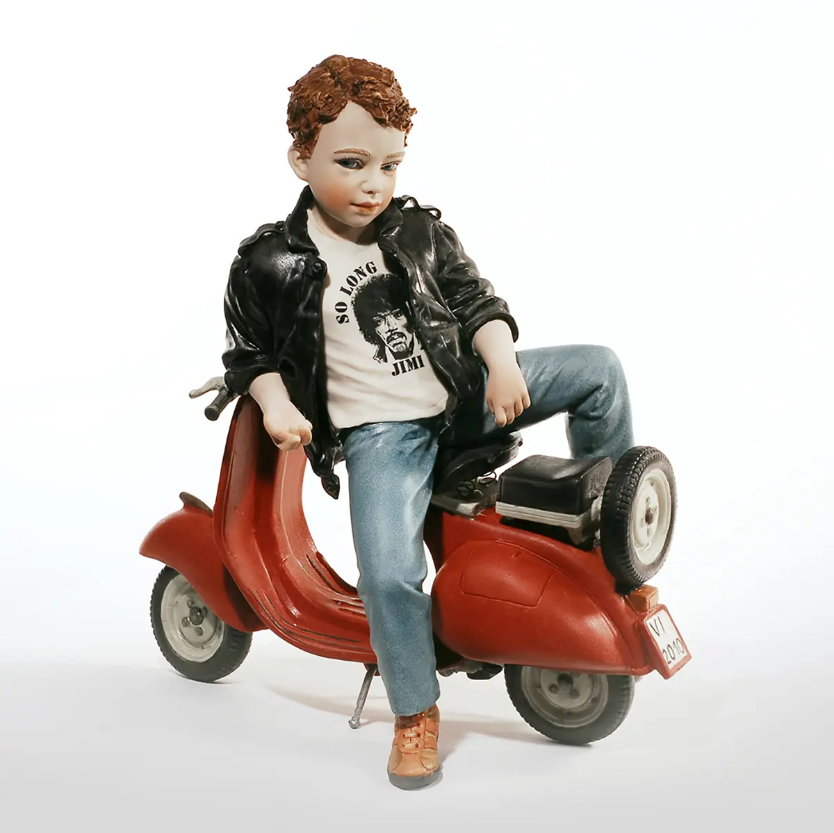 Statua in porcellana di un ragazzo in giacca di pelle nera e jeans seduto su una Vespa rossa.