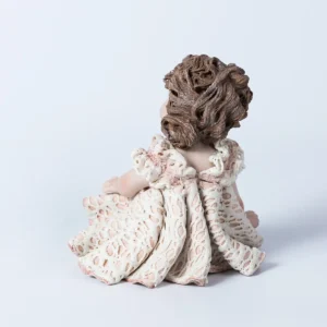 Statua in porcellana di bimba con abito in pizzo bianco e rosa, fiocco sul petto e capelli raccolti in uno chignon.
