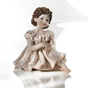 Statua in porcellana di ragazza seduta con abito rosa e bianco in pizzo e capelli raccolti in due chignon con fiocchi.