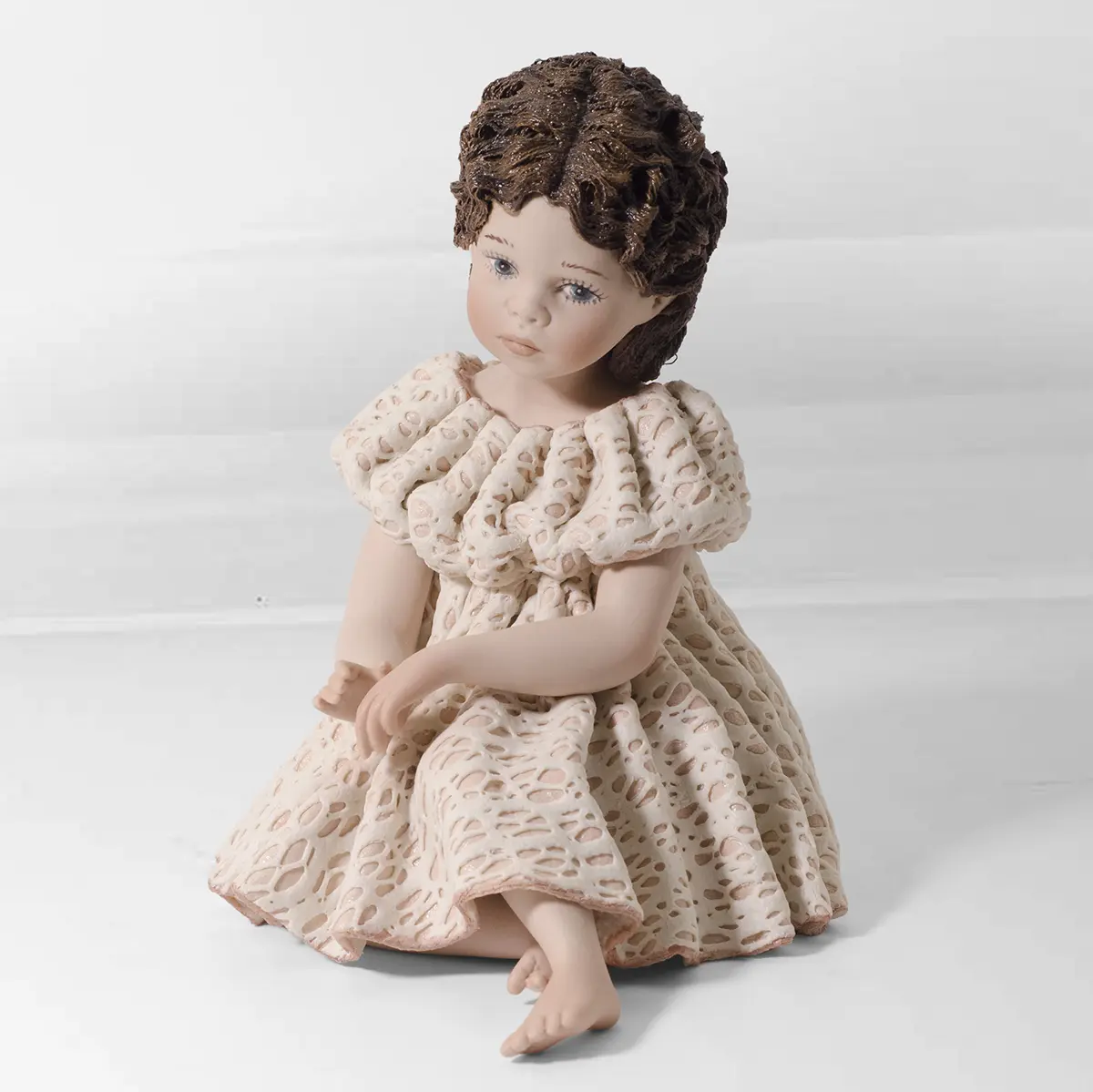 Statua in porcellana di ragazza seduta a terra con ampio abito in pizzo rosa e bianco e capelli con fiocchi rosa.