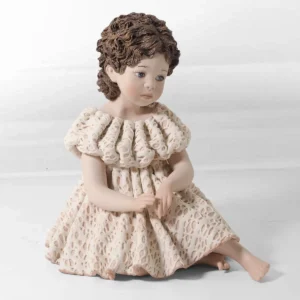 Statua in porcellana di ragazza seduta a terra con abito in pizzo rosa e bianco e chignon con fiocchi.