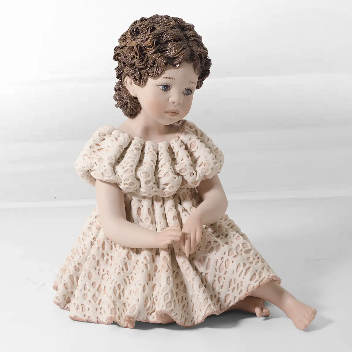 Statua in porcellana di ragazza seduta a terra con abito in pizzo rosa e bianco e chignon con fiocchi.