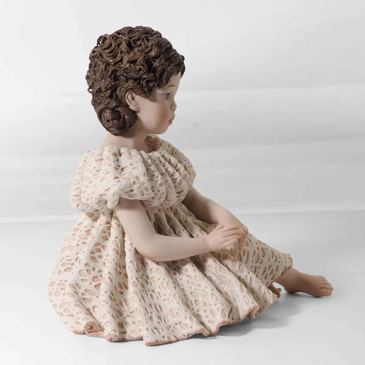 Statua in porcellana di giovane ragazza seduta a terra con abito rosa e bianco in pizzo e chignon con fiocchi rosa.