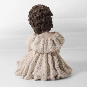 Statua in porcellana di ragazza in abito di pizzo rosa e bianco, seduta a terra con capelli raccolti in due chignon.