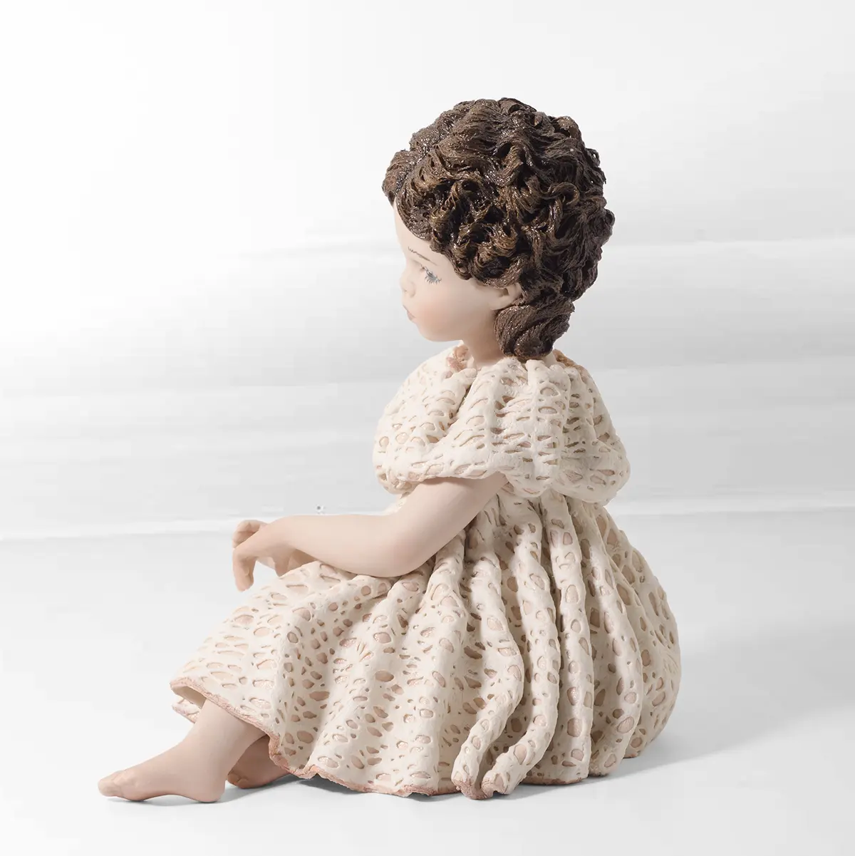 Statua in porcellana di ragazza seduta a terra con abito rosa e bianco in pizzo e due chignon con fiocchi rosa.
