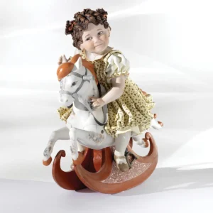 Statua in porcellana con bimba su cavallino a dondolo, abito giallo a fiorellini e capelli in due codine alte.