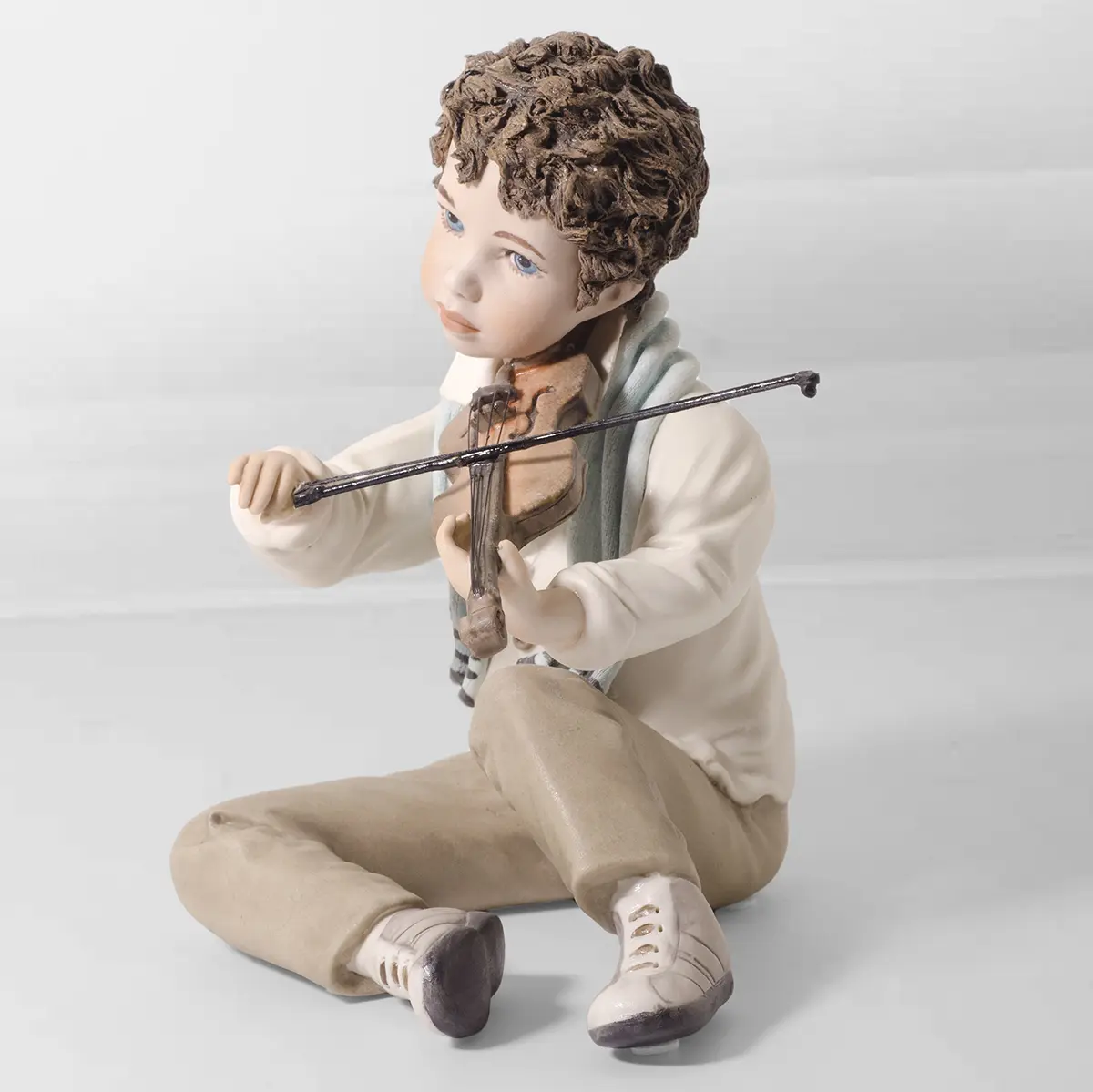 Statua in porcellana Tamino che suona un violino con camicia azzurrina, pantaloni marroni e sciarpa azzurra.