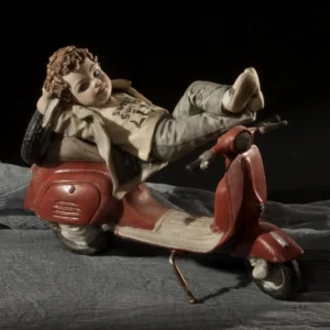Statua in porcellana di ragazzino steso con piedi sulla Vespa rossa, con maglia gialla, giacca color fango e jeans.