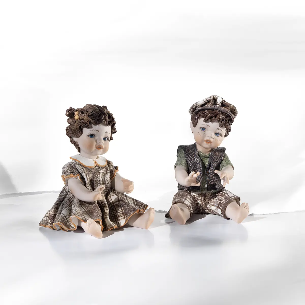 Statue in porcellana Sibania raffiguranti i bimbi Valentina e Tin Tin seduti a terra in abiti primaverili.
